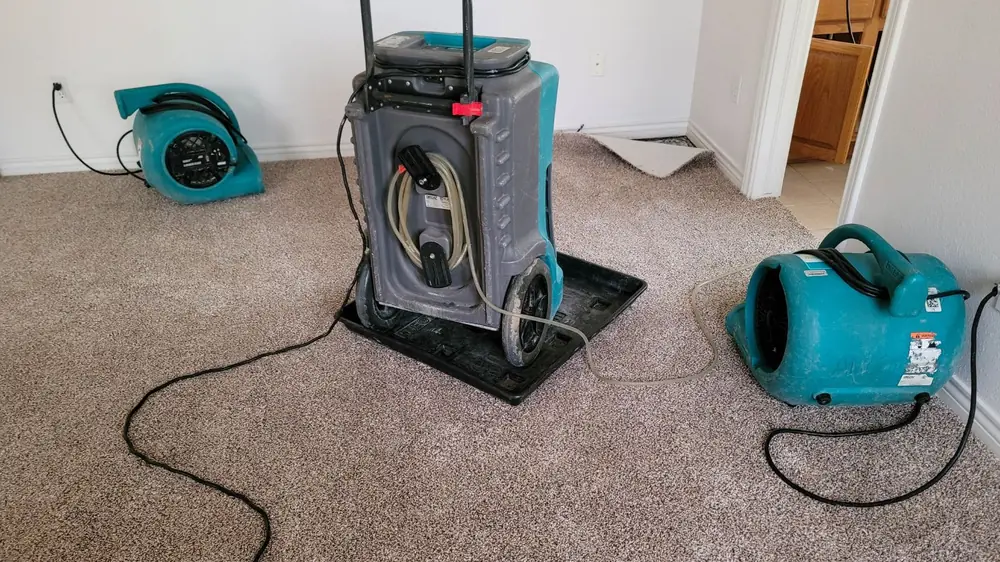 Air mover and dehumidifier drying carpet in an empty room