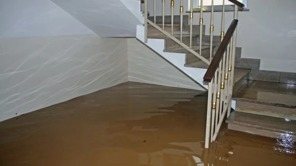 Brown floodwater covering a basement floor beside a staircase