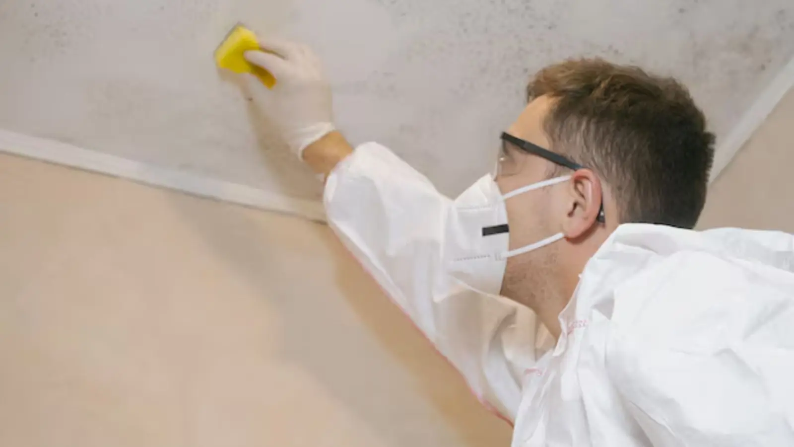 Worker in a mask wiping mold from a ceiling corner