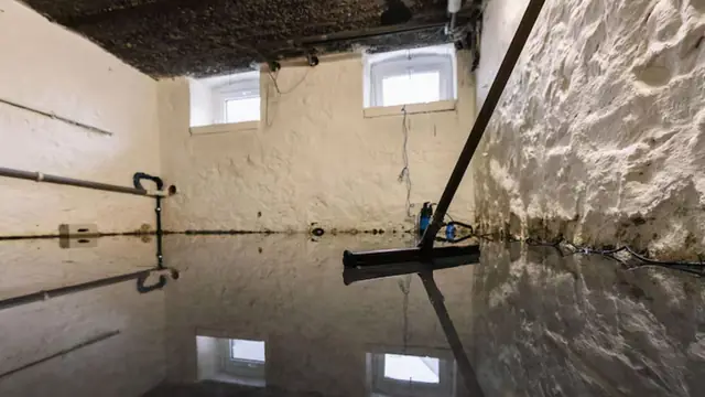Basement with standing water and a squeegee leaning on the floor