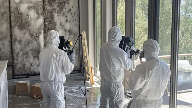 Crew in protective suits setting up equipment in a room with mold on the wall